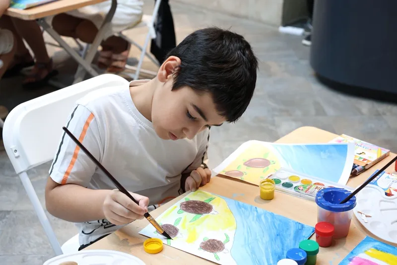 Enfant concentré sur une activité manuelle de peinture à une table en intérieur l'été